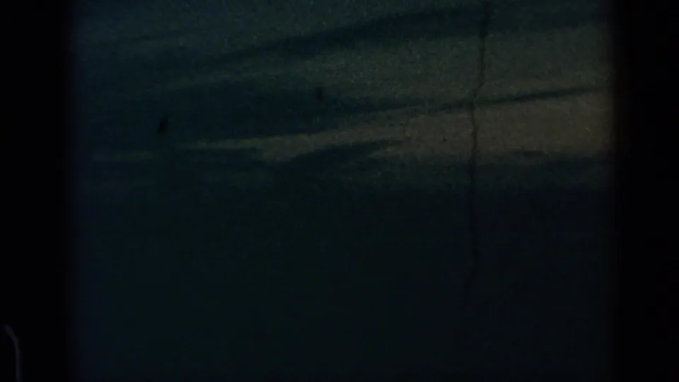 1960 8mm frame with dark blue-green sky, faint horizon streaking, dust or scratch marks, and black film-edge borders.