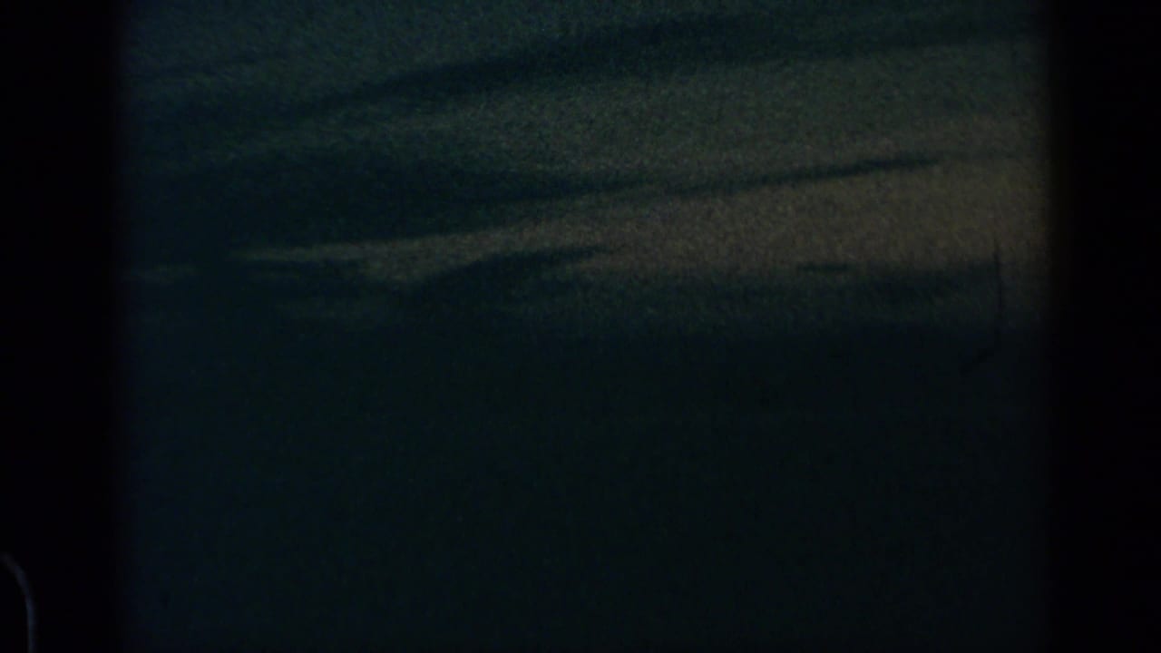 Dark airplane-window view over blue-gray evening clouds with grain and dust specks.