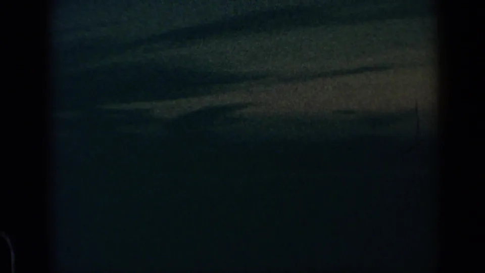1960 8mm airplane-window view over dim blue-gray cloud layers, with dark frame edges and visible film grain.