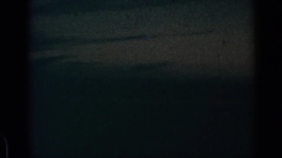 1960 8mm airplane-window view of a dark blue-gray cloudscape, with faint horizon detail and dust on the film.