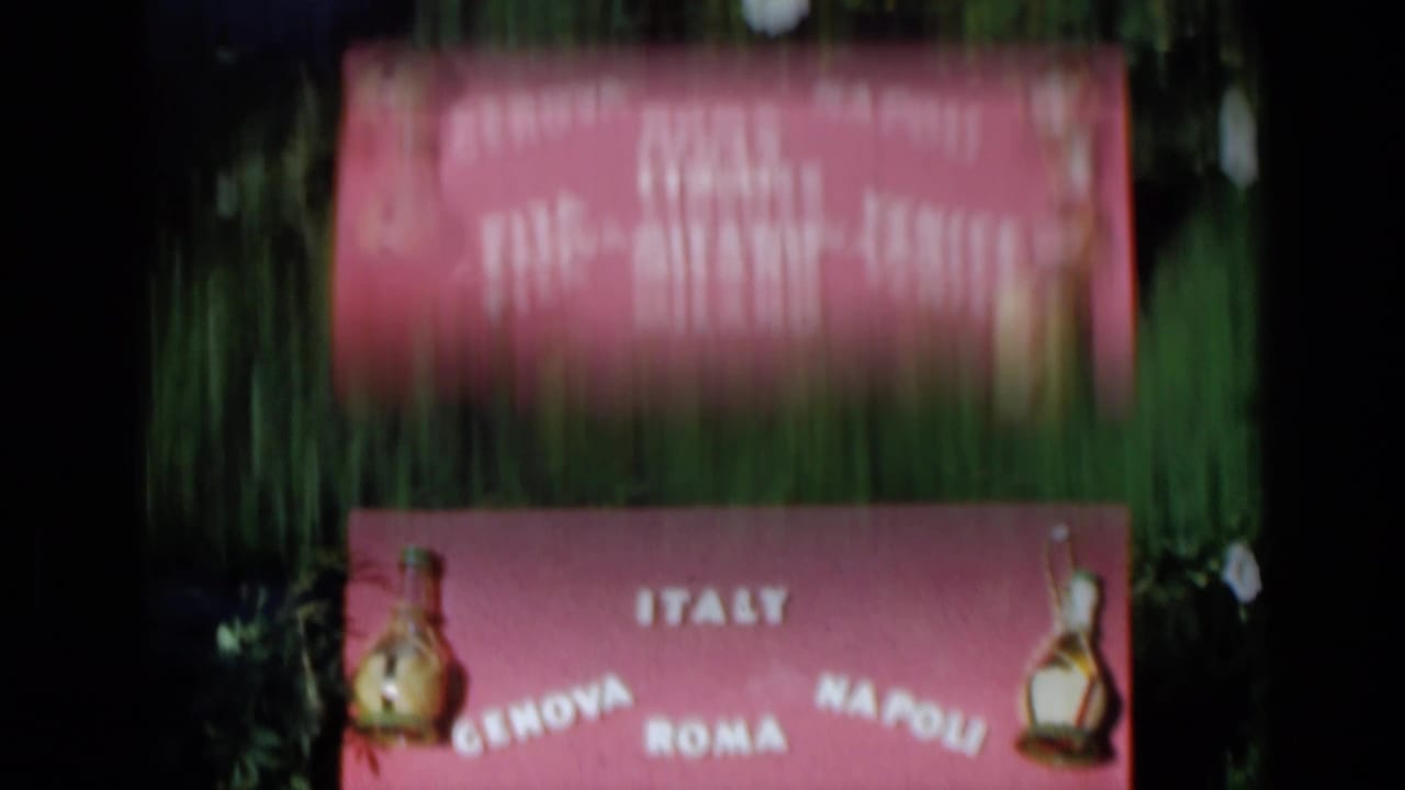 Pink sign with Italy and city names visible above grass and foliage.