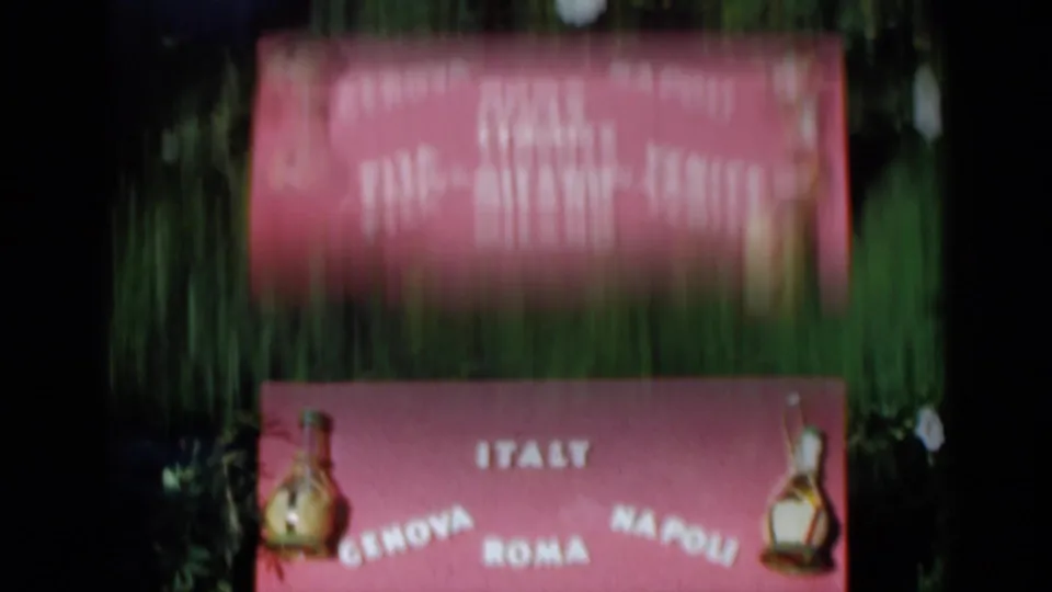 Pink Italian travel display in Venice, 1960, with city names and small carafe decorations amid greenery.