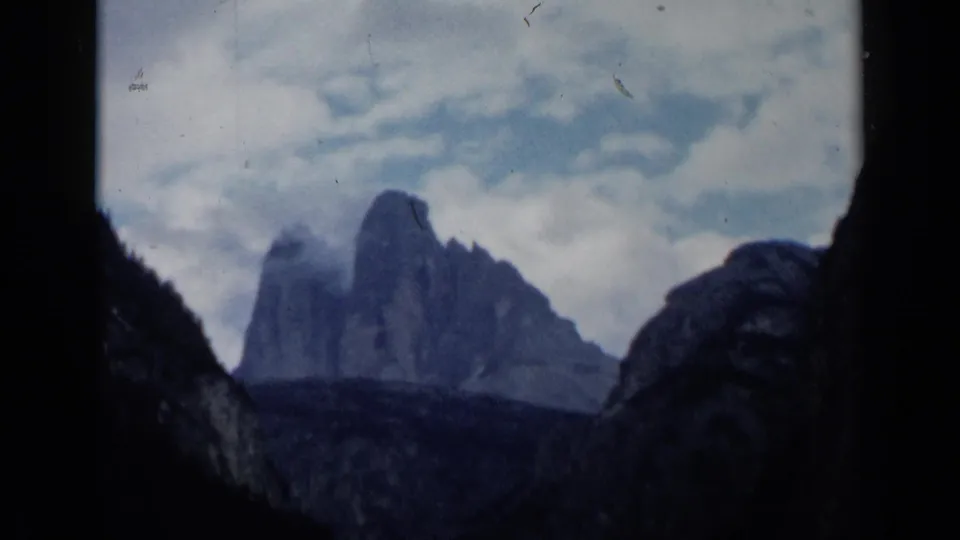 Vintage 8mm view of rugged Italian mountain peaks beneath a pale cloudy sky, with dark rock silhouettes along the sides.