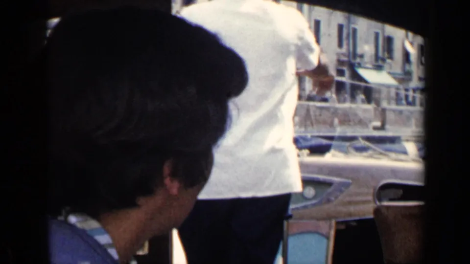 Inside-view frame from the Venice footage, with a passenger in the foreground and canal-side boats and buildings beyond.