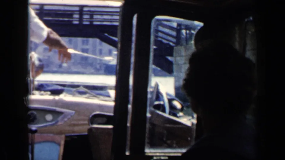 Passenger-level 1960 Venice canal footage showing a motorboat dashboard, windshield, and seated figure in shadow.