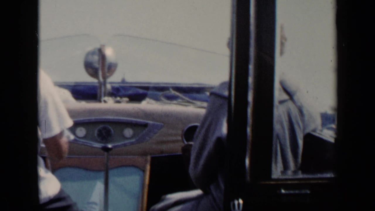 Passengers seen through dark framing beside a mid-century dashboard.