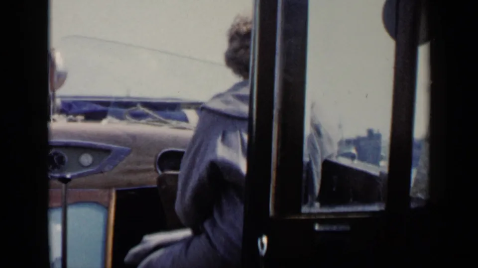 A seated passenger in a dark coat is filmed from behind inside transport during the 1960 Venice travel clip.