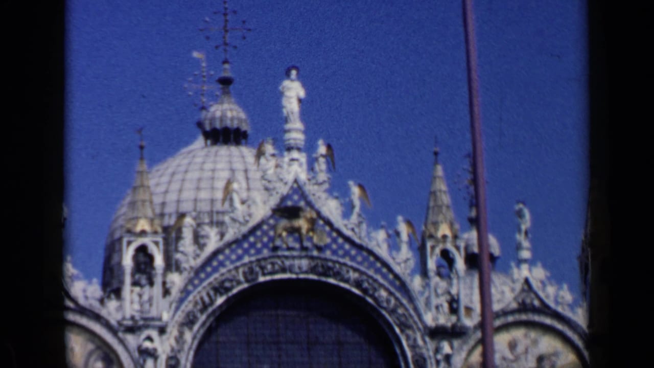 Upper facade of St. Mark's Basilica with dome, arch, statues, and blue sky.