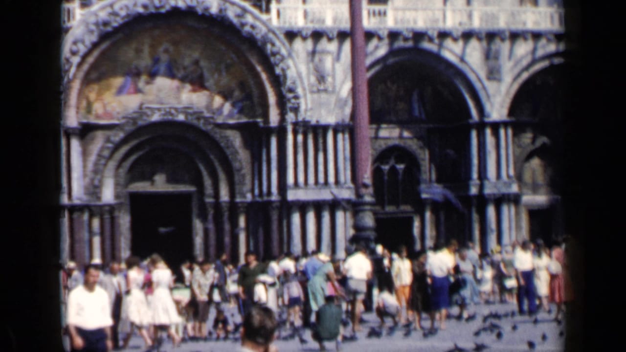Tourists stand before arched entrances and mosaics on St. Mark's Basilica.