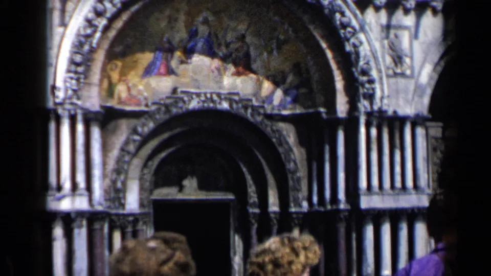 1960 Venice home-movie close-up of a St. Mark's Basilica portal with mosaic, dark entryway, columns, and visitor heads at the bottom edge.