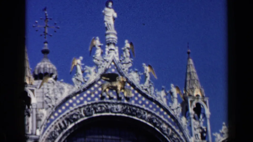 1960 Venice view of the winged lion of St. Mark, statues, spires, and patterned facade details against a saturated blue sky.