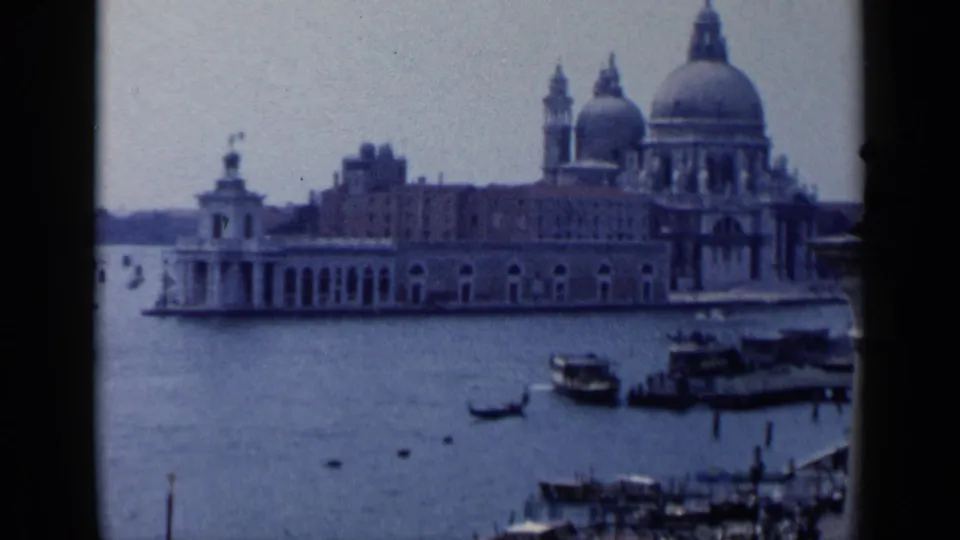 1960 8mm Venice canal view looking toward the domes of Santa Maria della Salute, with gondolas and small boats on the water.