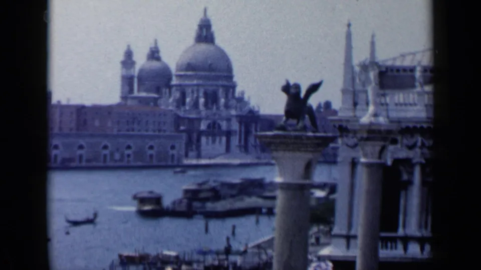 1960 Venice frame with Santa Maria della Salute in the distance, a winged lion column in the foreground, and mixed boat traffic on the water.