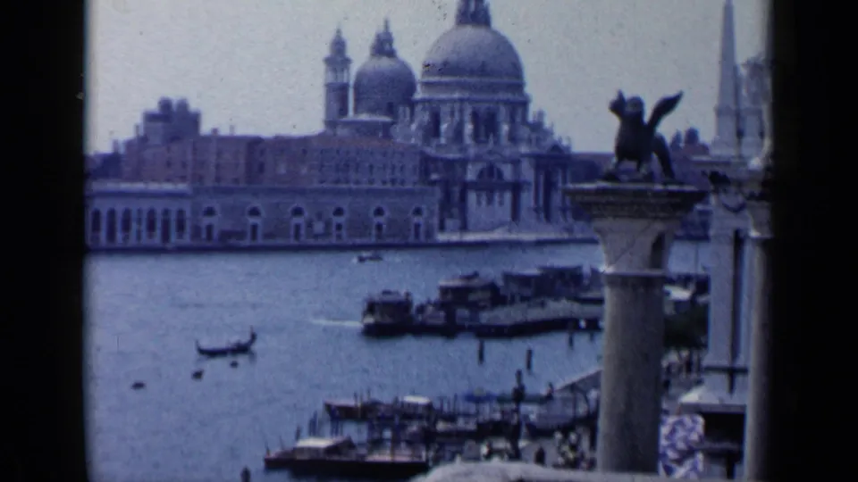 1960 Venice home-movie view across the lagoon, with the Salute domes, winged lion column, gondola, motorboats, and waterfront activity.