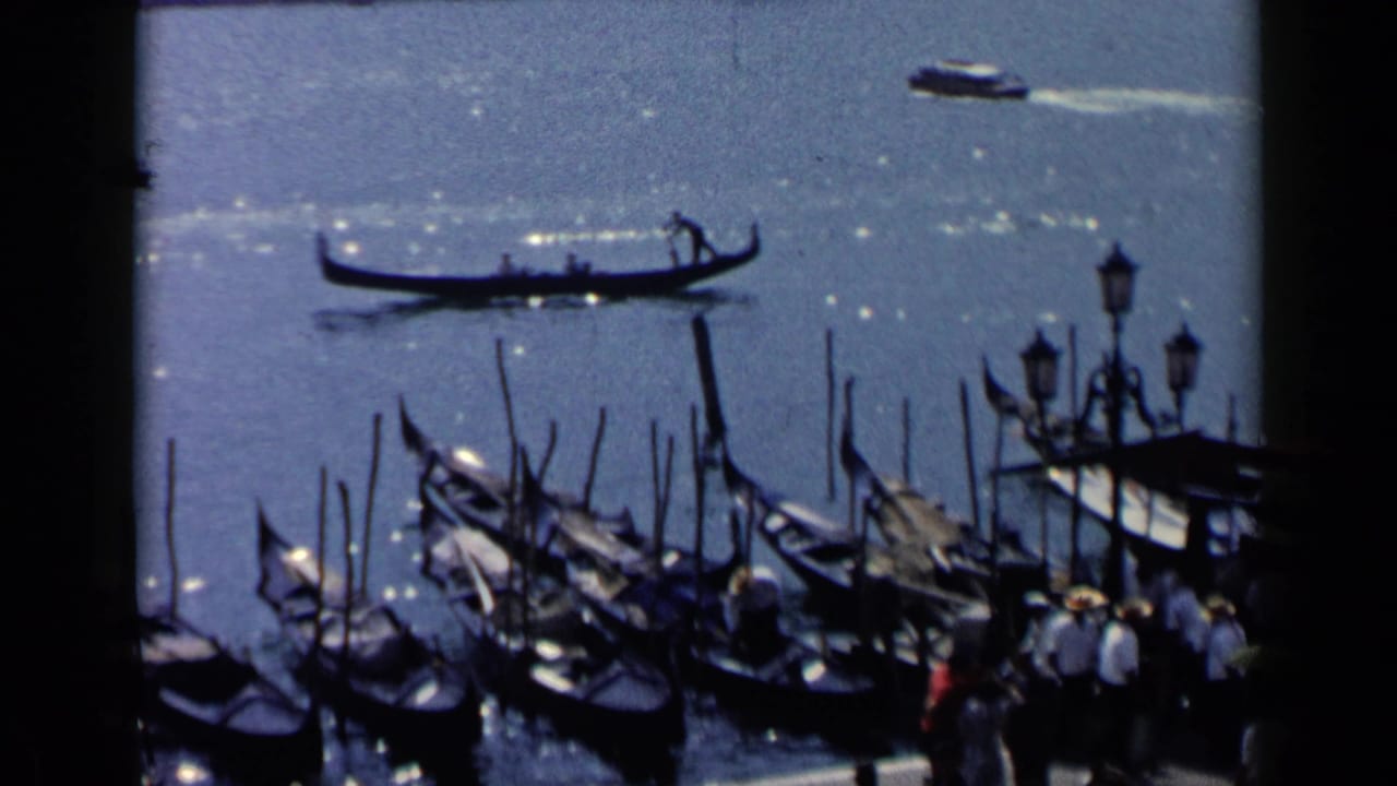 Gondolas and mooring poles on bright Venetian water, seen from an elevated viewpoint.