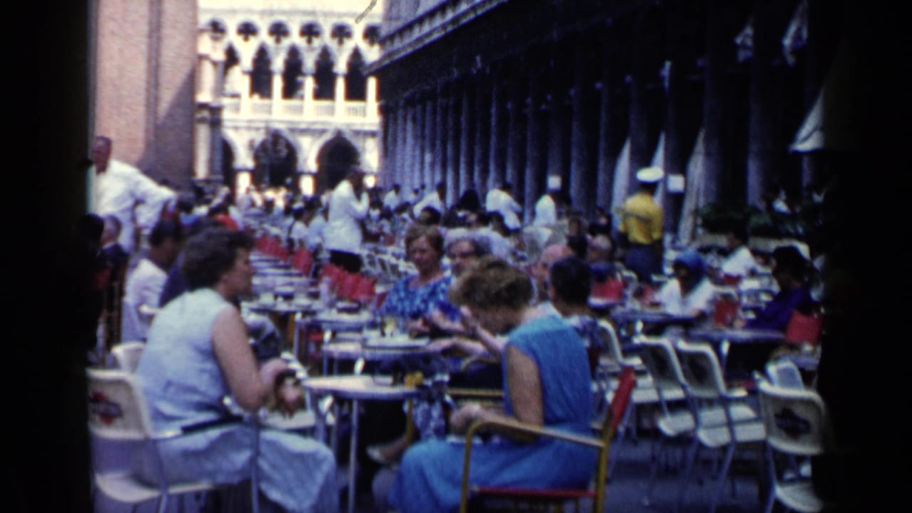 Crowded outdoor cafe with women seated at tables under a Venice colonnade.