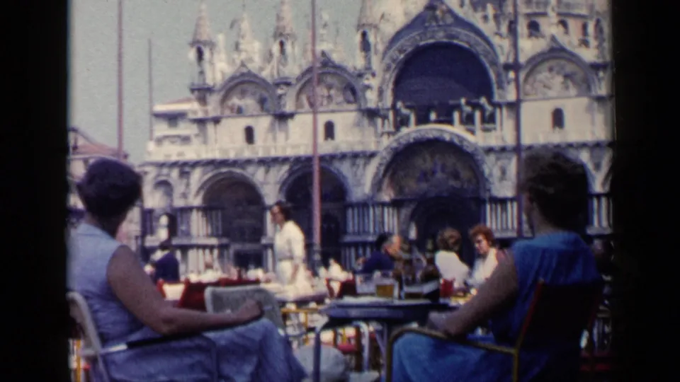 1960 Venice café view with seated patrons in the foreground and Basilica di San Marco visible behind the outdoor tables.