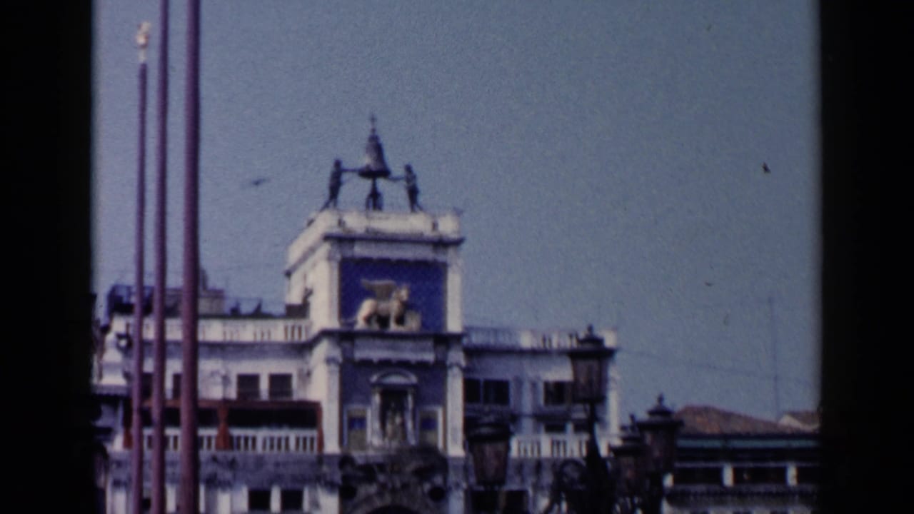 Upper portion of the St. Mark's Square clock tower with flagpoles at left.