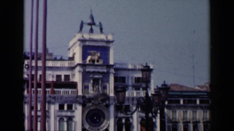1960 Venice footage shows more of the St. Mark's Square clock tower facade, including the clock face and surrounding architecture.