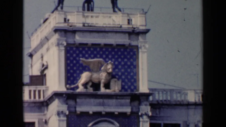 1960 Venice close framing of the winged lion sculpture on a historic facade with blue patterned panels and surrounding stonework.