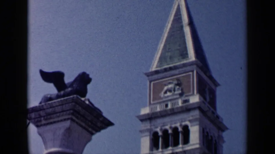 1960 Venice 8mm frame with the bell tower spire and column-mounted winged lion seen from a low visitor angle.