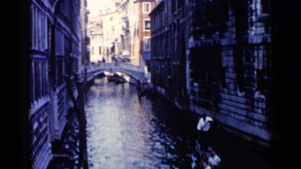 1960 Venice frame showing a gondolier at the lower right with passengers as the canal recedes toward an arched bridge.