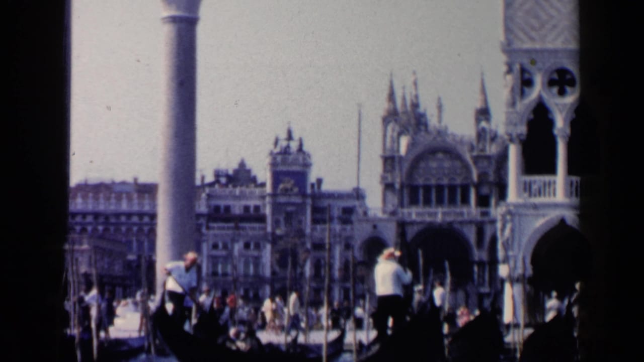 Gondoliers row black gondolas on a crowded Venetian waterway near ornate buildings and columns.