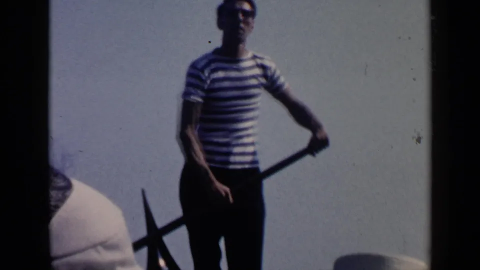 1960 Venice frame with a standing gondolier in a striped shirt holding an oar beside the gondola.
