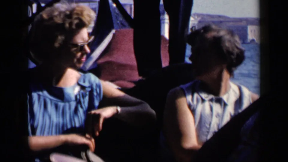 1960 Venice home-movie frame showing women passengers seated in a gondola during a canal ride.