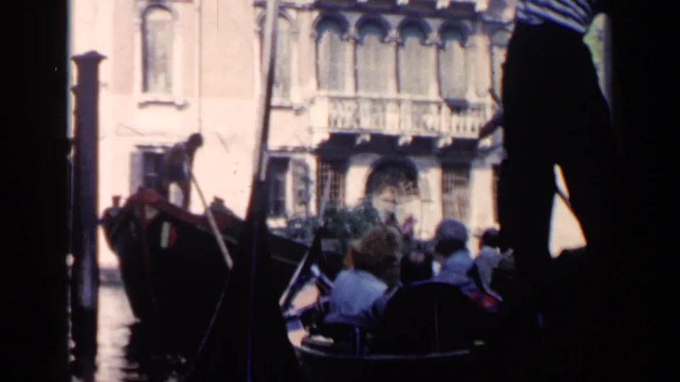 1960 Venice frame showing gondola passengers on the canal with historic building facades in the background.