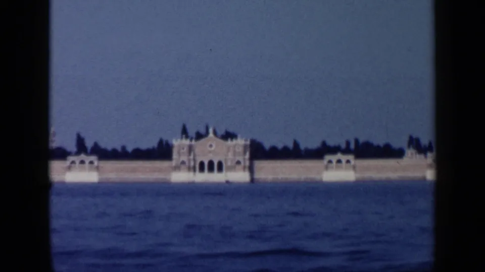 1960 Venice home-movie frame showing a distant grand waterfront building across the lagoon or canal.