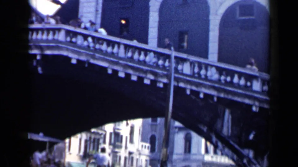 1960 Venice frame showing pedestrians on the Rialto Bridge and canal-side architecture beyond.