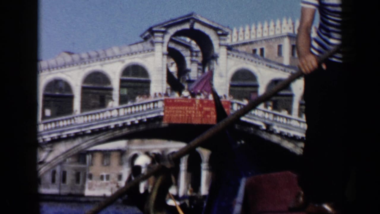 Gondolier rowing in front of the Rialto Bridge and canal buildings.