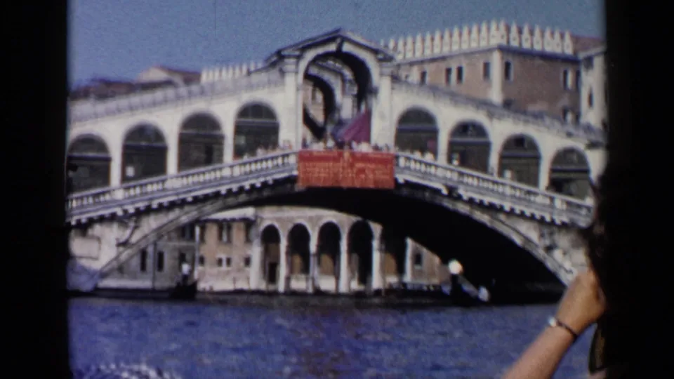 1960 8mm Venice wide frame of the Rialto Bridge spanning the canal, with part of a passenger visible at the lower right.