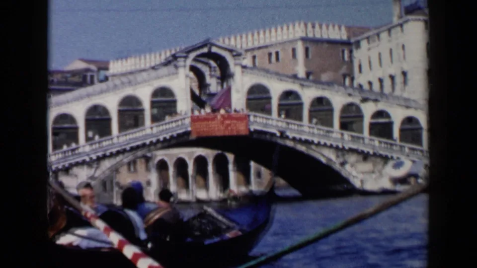 1960 Venice gondola scene with tourists in the lower frame and the Rialto Bridge spanning the Grand Canal behind them.