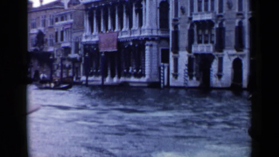 Soft 8mm view from a gondola toward canal-side Venetian buildings and rippling water in Venice.