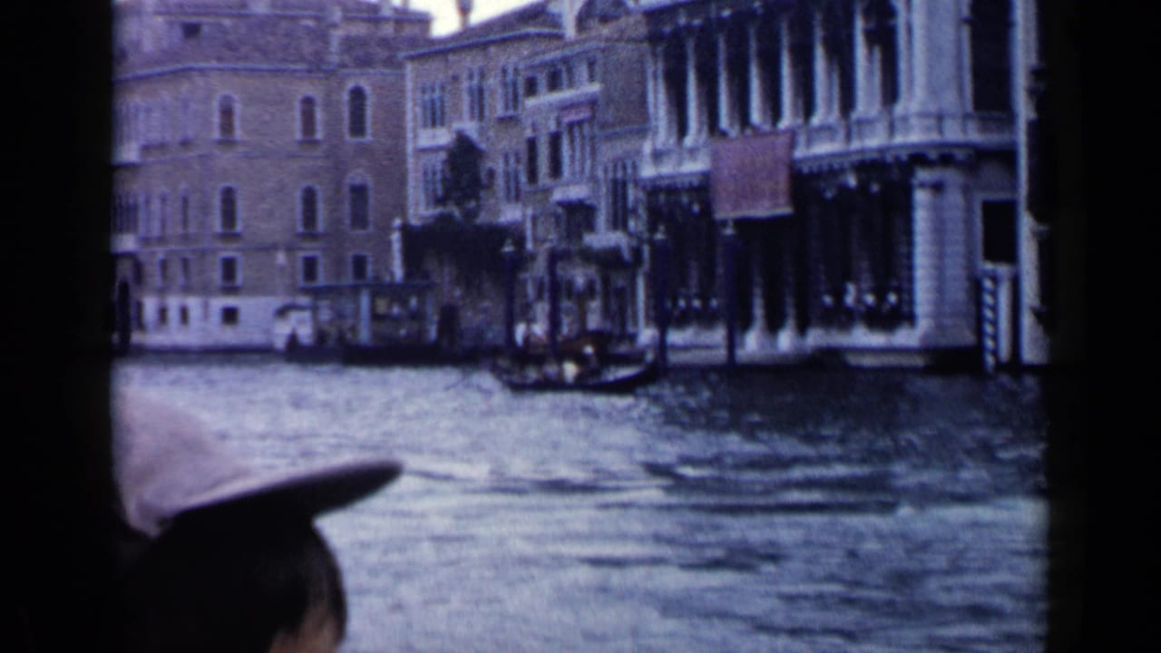 Grand Canal view with waterfront buildings, gondolas, and a partial hat silhouette in the foreground.