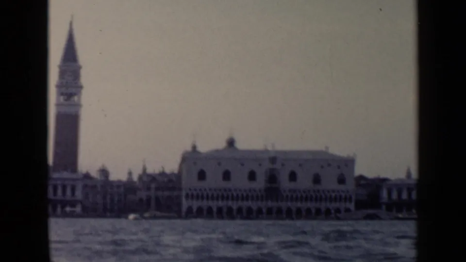 1960 Venice home-movie frame showing the Campanile and Doge's Palace from a moving boat on the water.