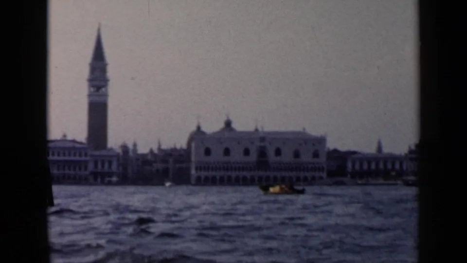 1960 8mm Venice waterfront view with the Campanile, Doge's Palace, rippled water, and a small gondola.