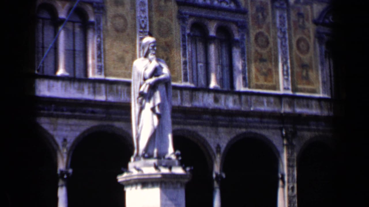 1960 Venice 8mm frame showing a white robed statue on a pedestal in front of arched colonnades and patterned facade panels.