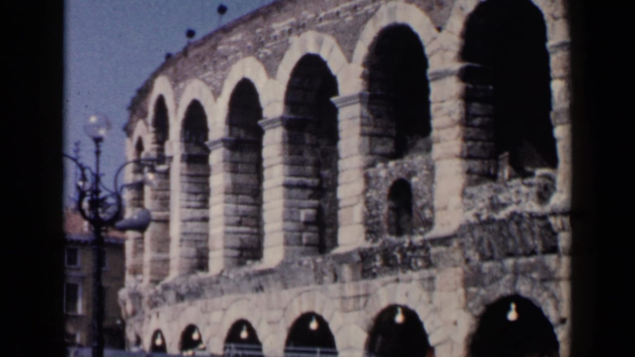Roman amphitheater facade with a globe lamppost near the left edge.