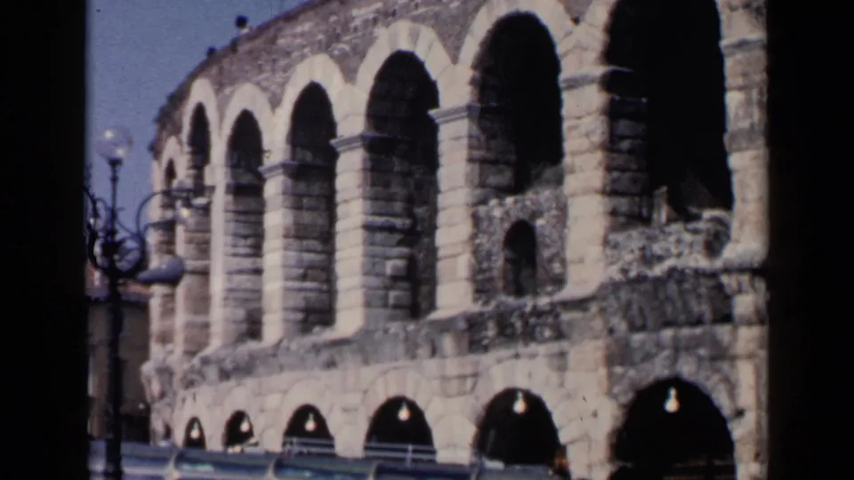 1960 8mm frame of the Roman amphitheater facade, emphasizing repeating arches and aged masonry.
