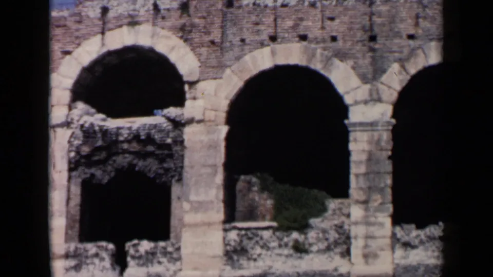 1960s 8mm travel frame showing weathered stone arches and dark openings, likely near an Italian historic site.