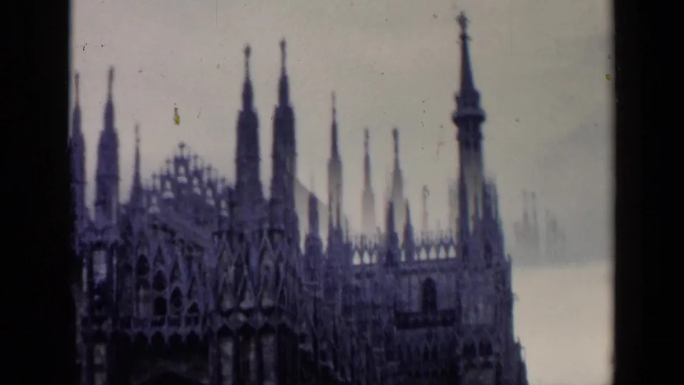 Milan Cathedral appears from an angled 1960s 8mm view, showing spires, tracery, and a pale sky beyond the facade.