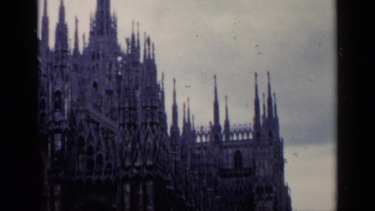 Upper section of an ornate church facade with spires silhouetted under clouds.