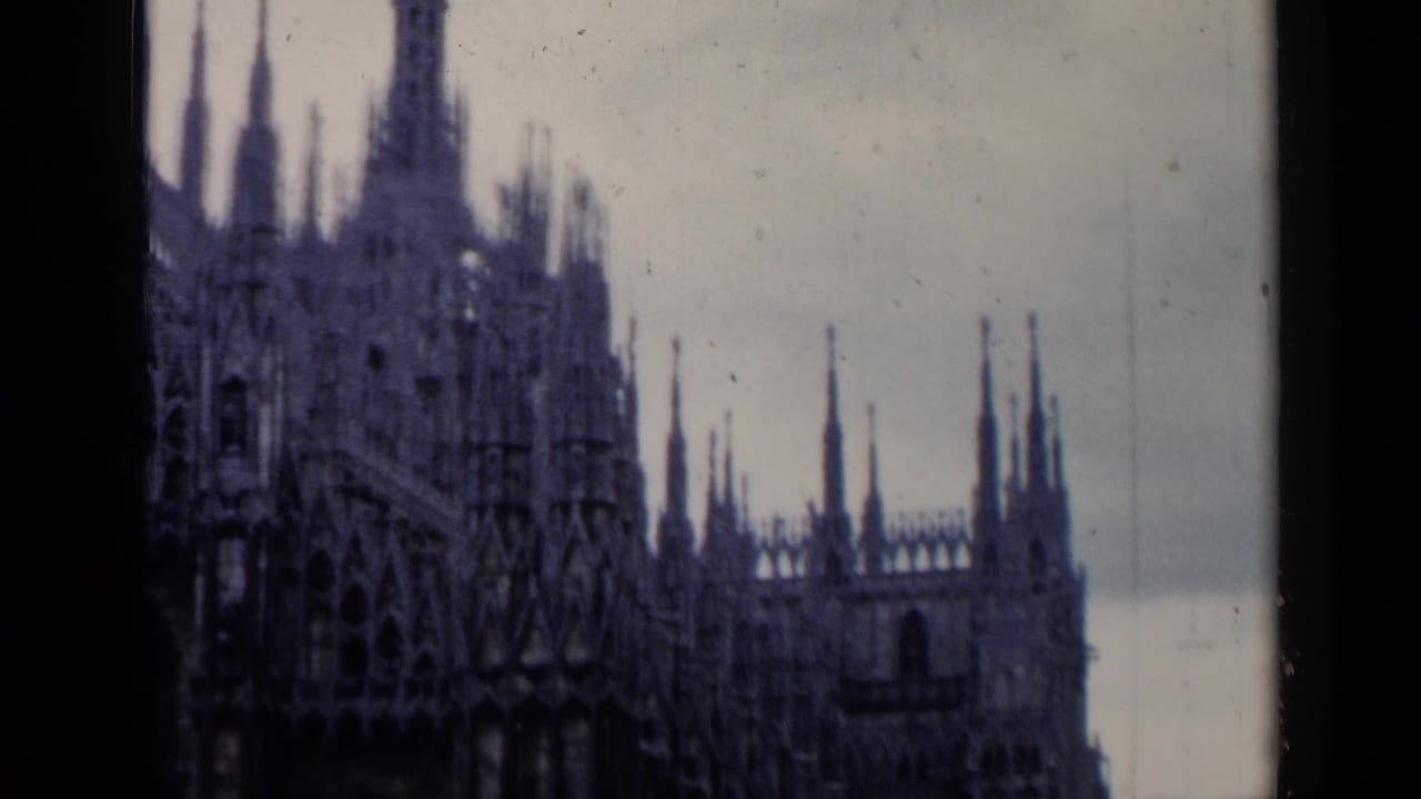 Dark 8mm view of a Gothic cathedral facade with many spires against a pale sky.