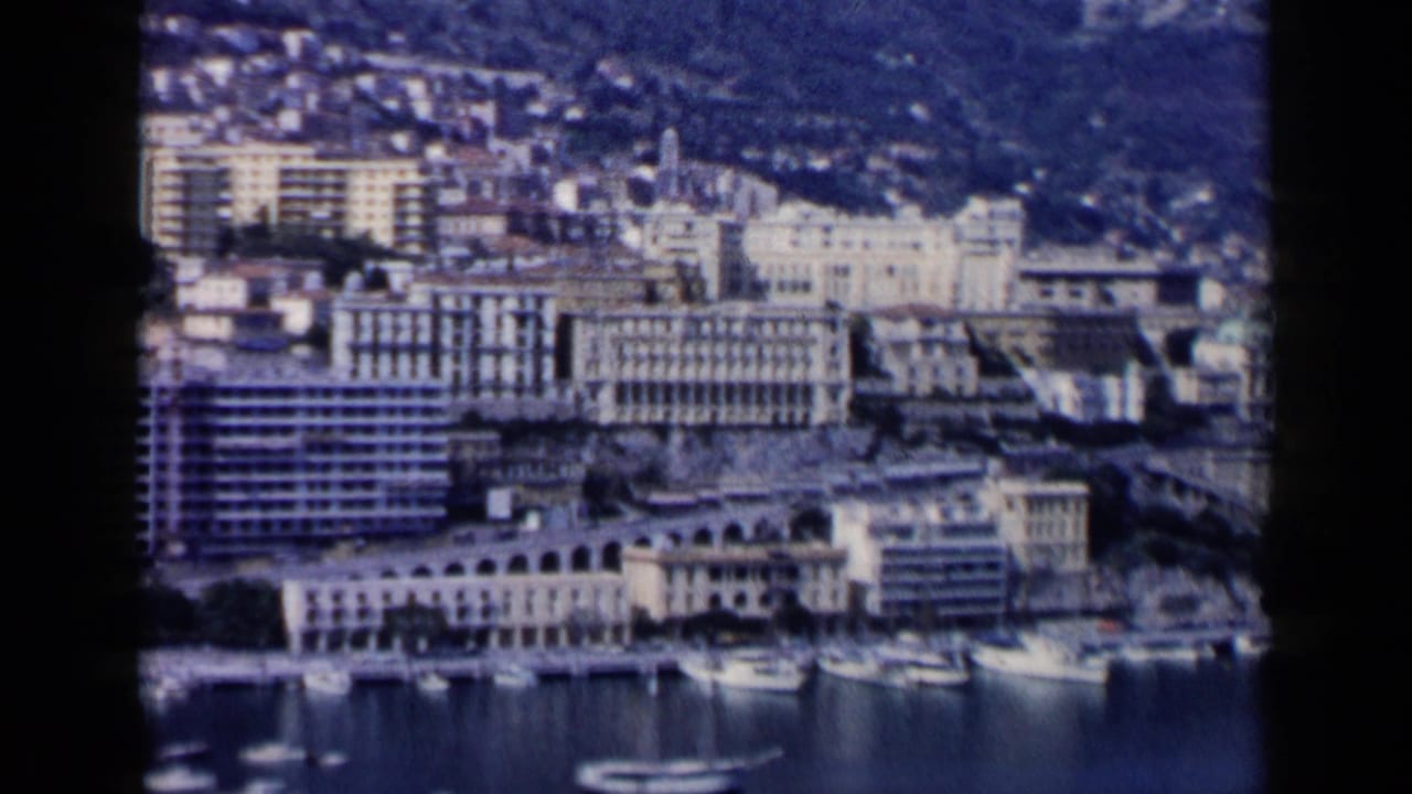 Elevated view of a harbor city with boats, waterfront buildings, and hillside development.