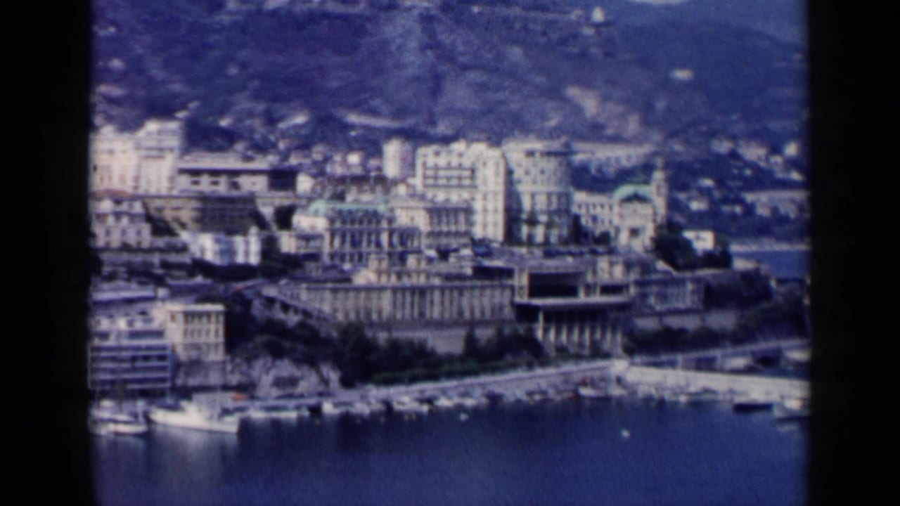 Distant waterfront buildings beside blue harbor water with hills behind.