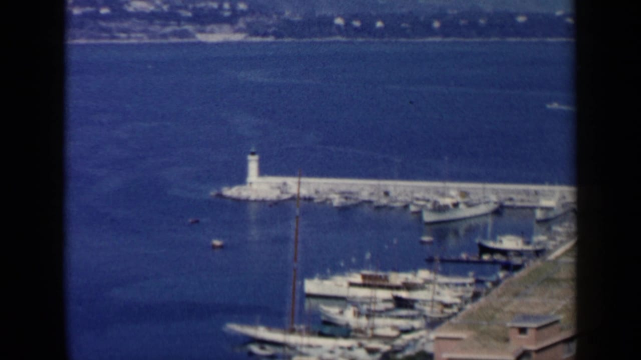 Blue harbor water with a white breakwater, small lighthouse, docked boats, and distant shoreline.