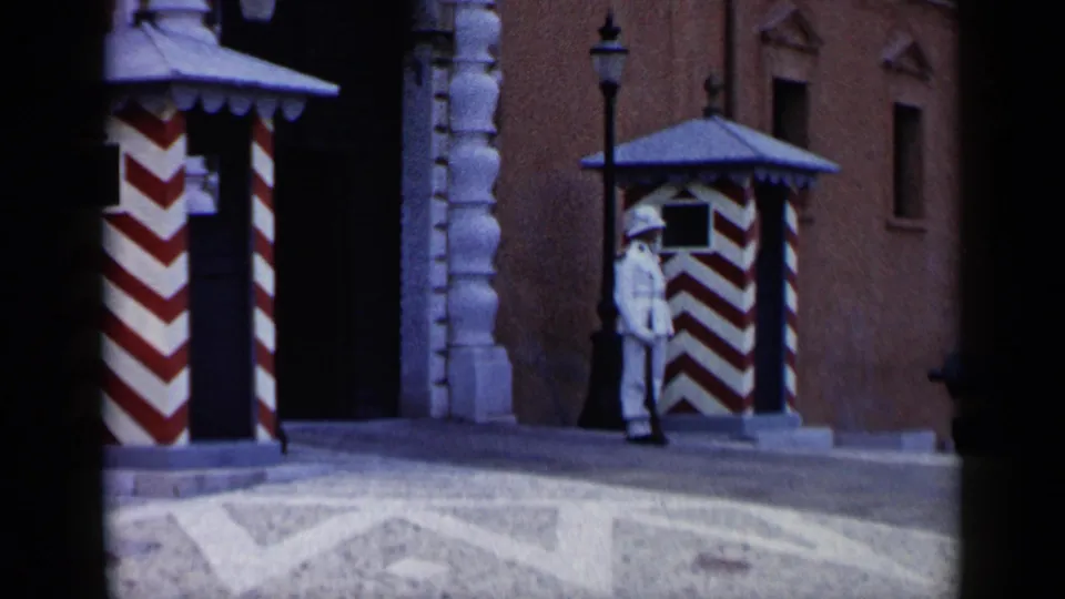 1960 Venice frame showing a uniformed guard at attention beside red-and-white striped booths and a historic facade.